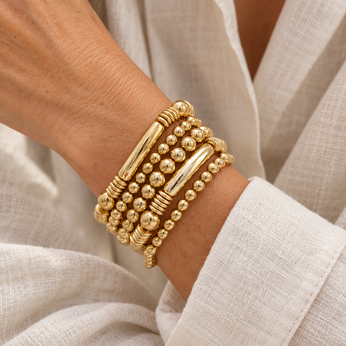 Five gold beaded bracelets on a woman’s wrist