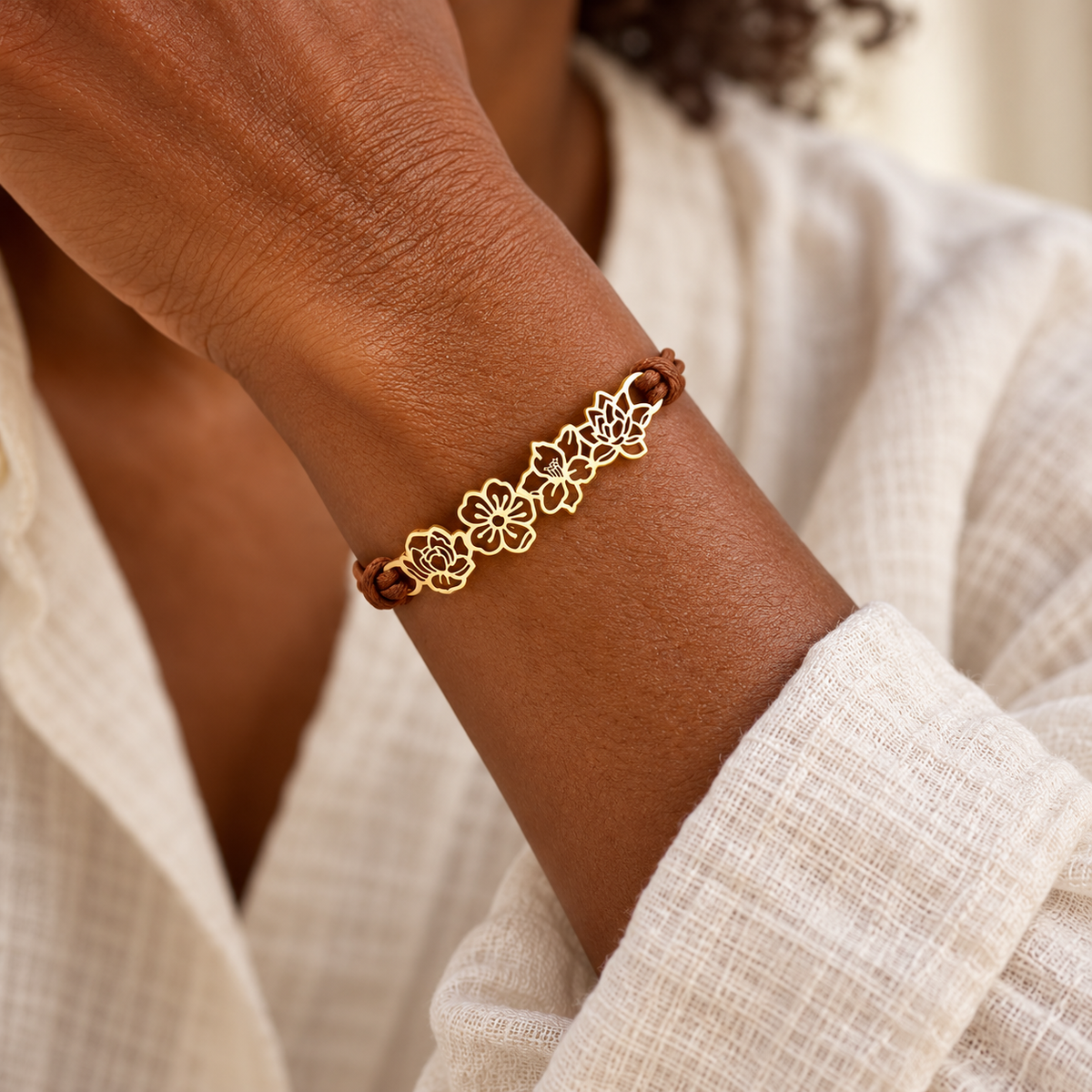 Gold floral bracelet with brown cord on a woman's wrist