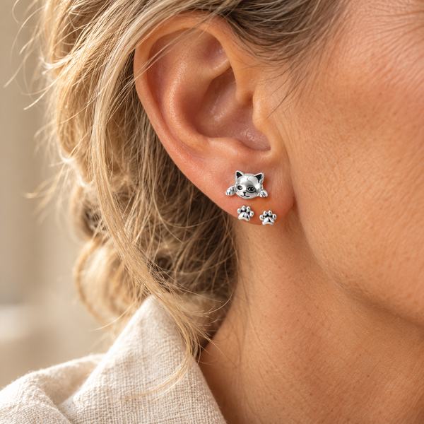 Silver cat and paw stud earrings worn in an ear