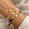 Three heart charm bracelets in pink white and black on a woman’s wrist
