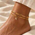 Two gold anklets with a K charm on a woman's ankle