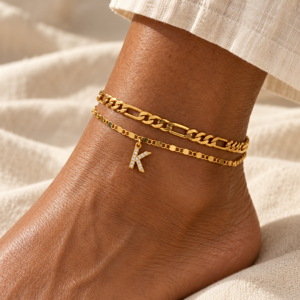 Two gold anklets with a K charm on a woman's ankle